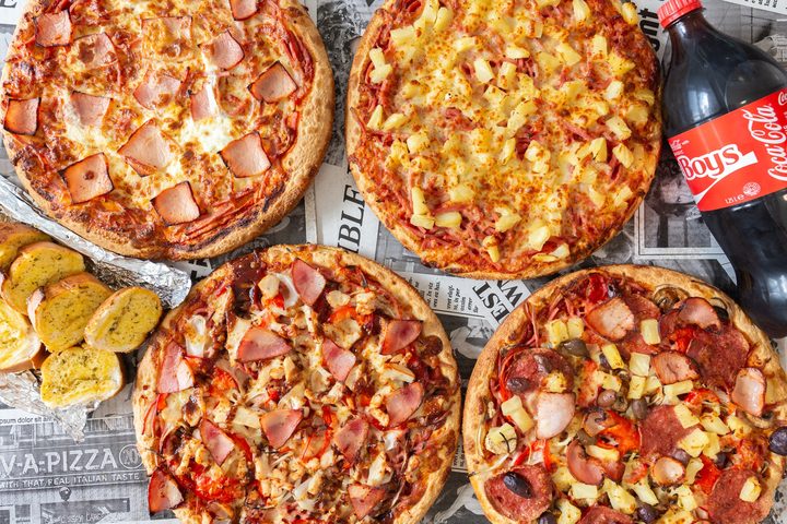 Four large pizzas, garlic bread and a bottle of Coke laid out on newspaper-print paper