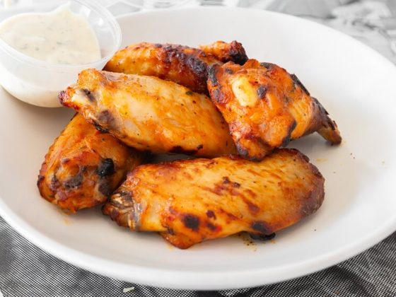 Chargrilled chicken wings on a white plate with a pot of creamy dipping sauce
